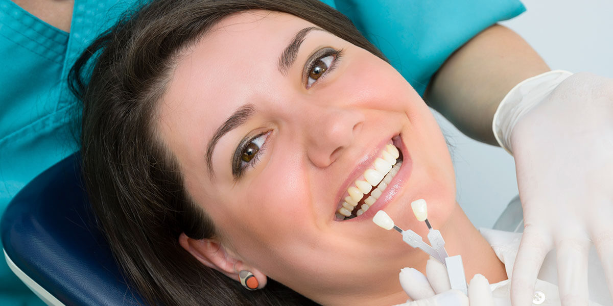 Woman smiling while having her tooth color matched to a bonding shade guide