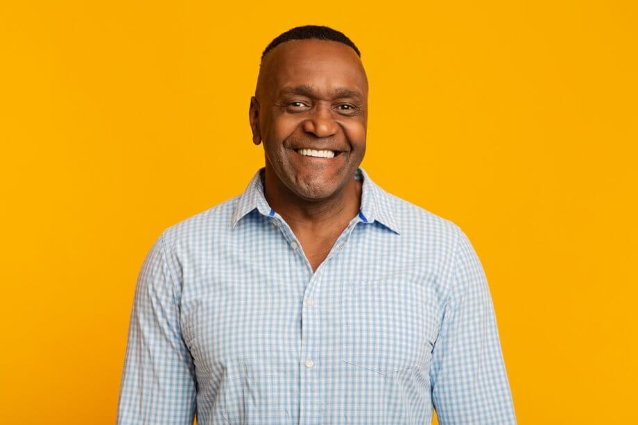 older man smiling wearing a blue and white plaid button down shirt