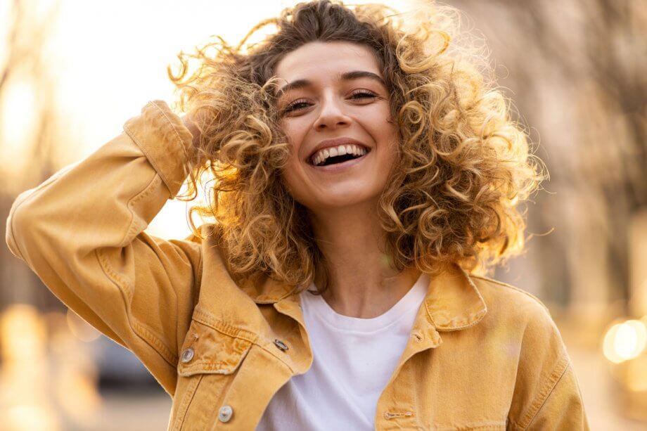 smiling young woman with blonde curly hair wearing a yellow jean jacket